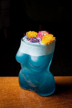 A unique blue cocktail in a sculptural glass, topped with colorful flowers, charms the night.の写真素材