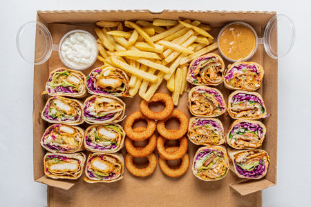 A delicious assortment of wraps, fries, and onion rings arranged in a takeout box awaits enjoyment.の写真素材