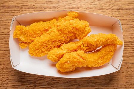 Scrumptious chicken tenders coated in crispy breading are served in a simple white box.の写真素材