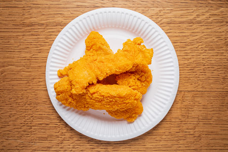 Deliciously fried chicken tenders are neatly arranged on a paper plate, inviting for a tasty meal.