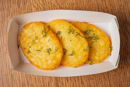 A platter displays four perfectly fried fritters topped with vibrant green dill.