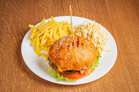 A hearty burger with fresh ingredients alongside crispy fries and tangy coleslaw on a rustic table.の写真素材