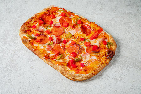 Delicious rectangular pizza topped with peppers, ham, and fresh tomatoes, ready to enjoy!の写真素材