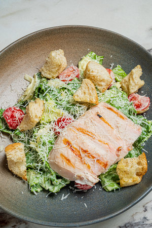 Freshly prepared grilled salmon rests on a vibrant bed of greens, croutons, and cheese.の写真素材