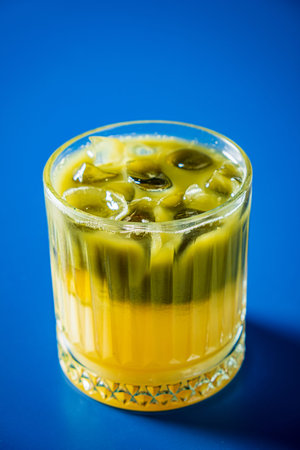 A glass showcases a colorful drink with distinct layers and a touch of ice, capturing attention.
