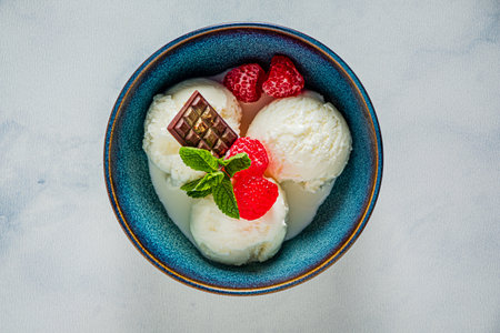 Three creamy scoops of vanilla ice cream with strawberries, chocolate, and mint elevate desserts.の写真素材