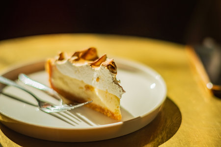 A slice of lemon meringue pie on a plate invites sweet indulgence in warm light.の写真素材