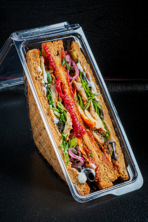 A vibrant sandwich with fresh layers is artfully arranged in a clear container.の写真素材