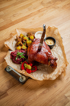 A generous serving of roasted meat accompanied by crispy potatoes, colorful vegetables, and sauces.の写真素材
