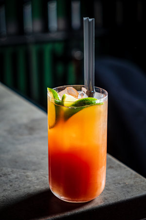 Brightly colored drink with lime slices and ice resting on a textured surface, inviting relaxation.の写真素材