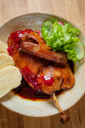A beautifully presented roast duck glistens with sauce, surrounded by bread and fresh greens.の写真素材