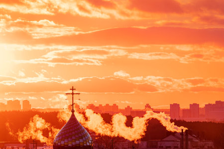 Vibrant colors illuminate the sky at sunset, with smoke wafting from city buildings.の写真素材