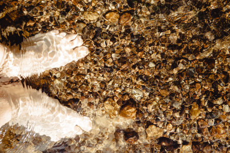 Soft sunlight dances on the clear water, where bare feet touch smooth pebbles, inviting peace.