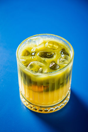 A colorful glass filled with a tropical drink sits on a bright blue surface, inviting refreshment.