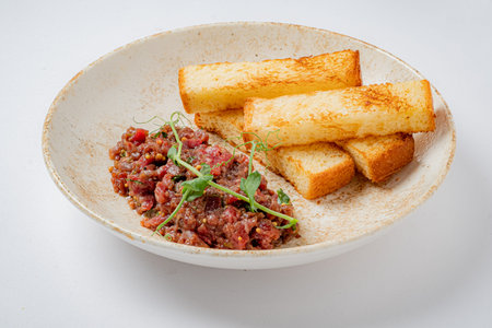 Juicy minced meat served alongside crispy toasted bread, garnished with fresh herbs for flavor.の写真素材