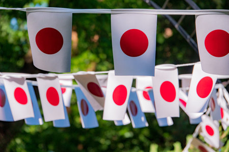 Banners adorned with vivid red circles sway gently among lush greenery during a lively gathering.