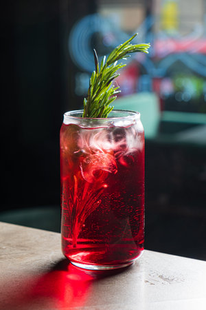 Bright red beverage with a sprig of herb sits on a wooden table in a lively urban bar atmosphere.