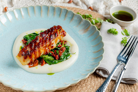 Tender grilled fish atop smooth puree surrounded by vibrant greens and a drizzle of sauce.