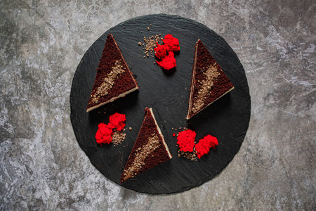 Three elegant chocolate cake slices arranged on a dark slate board with vibrant red garnishes.