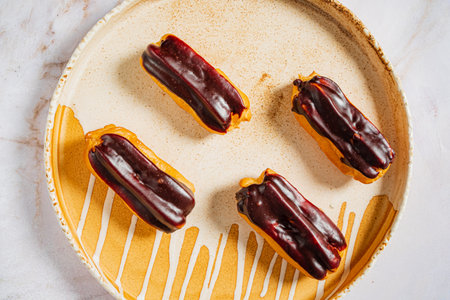 Four glazed eclairs on an elegant dish, showcasing their tempting colors.