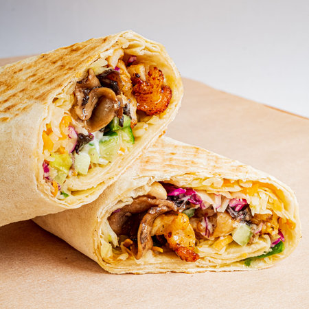 Tasty burrito filled with shrimp, mushrooms, and fresh vegetables placed on a light background.