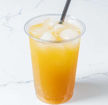 A tall cup of iced tea glistens with ice cubes, reflecting colors on a smooth marble table.の写真素材