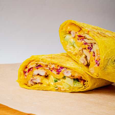 Two colorful chicken and veggie wraps with cheese lie on a wooden surface, tempting you.の写真素材