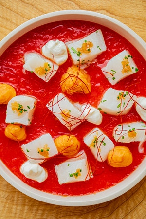 A colorful dessert features creamy squares floating atop a vibrant red sauce, garnished artfully.の写真素材