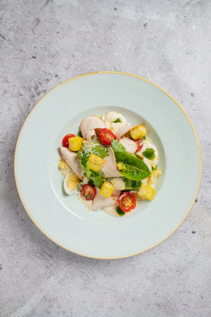 A colorful chicken salad featuring cherry tomatoes, corn, and leafy greens on a pale plate.