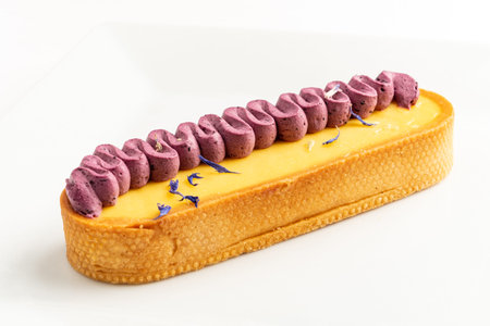 A vibrant lemon tart showcases bold purple berry cream, beautifully garnished with delicate flowers.