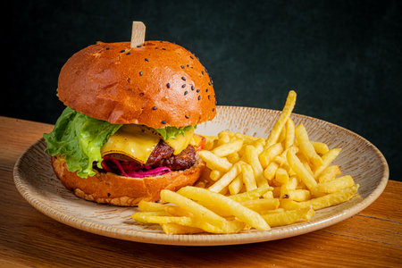 Delicious beef burger topped with cheese, lettuce, and pickles, accompanied by crispy fries.の写真素材