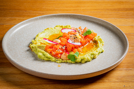 A vibrant plate of creamy guacamole topped with tomatoes, radish, and herbs.の写真素材