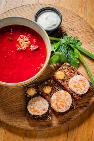 A colorful beet soup paired with rye bread topped with cheese and served with fresh herbs.の写真素材