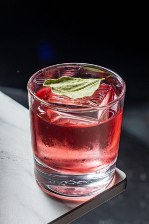 A refreshing red drink with large ice and a leaf garnish sits ready to drink.