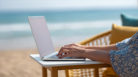 A woman focuses on her laptop, enjoying the beach view and warm sunlight around her.の素材