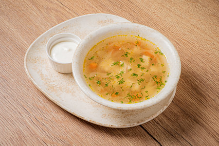 Savory chicken soup with veggies and herbs, plus a small dish of cream.の写真素材
