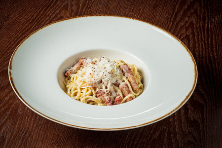 Spaghetti carbonara topped with cheese and pepper sits invitingly in a stylish bowl.の写真素材