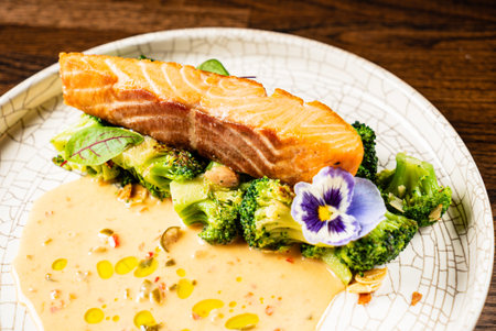 Succulent salmon rests atop fresh broccoli and a creamy sauce, beautifully garnished with a flower.