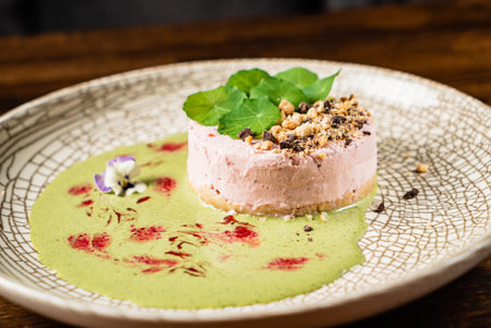 A beautiful dessert featuring layers of berry mousse with green sauce, nuts, and flower garnish.の写真素材