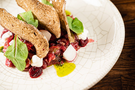 Delicious beef tartare elegantly plated with colorful radish slices and crunchy bread chips.の写真素材