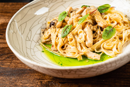 A hearty bowl of pasta featuring savory chicken and herbs, nestled on a wooden table.の写真素材