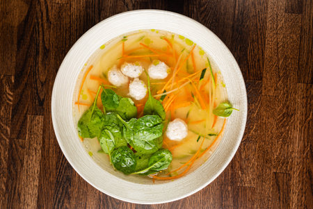 Bowl of broth with fresh spinach and colorful veggies on a wooden table.の写真素材