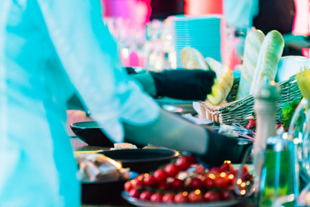 A waiter in gloves serves drinks while arranging colorful vegetables for guests at an event.の写真素材