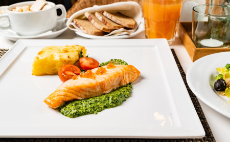 A delicious salmon fillet is elegantly presented on a plate with green sauce and fresh veggies.の写真素材