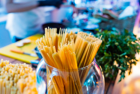 Pasta stands tall in a glass container as friends gather to cook a delightful meal together.の写真素材