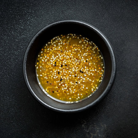 A small black bowl holds honey sesame vinaigrette with golden dressing and sesame seeds.の素材