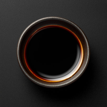 Rich, dark soy sauce in a small black bowl contrasts with the sleek, black surface.の素材