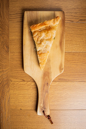 A fresh slice of flaky pastry sits on a wooden board, inviting and warm, in a homely kitchen.