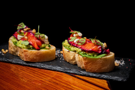 Delicious avocado toast garnished with roasted vegetables and fresh herbs sits on a stylish slate.
