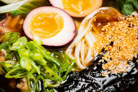 Enjoy rich ramen with soft eggs, fresh greens, and sesame seeds in a tasty broth.の写真素材